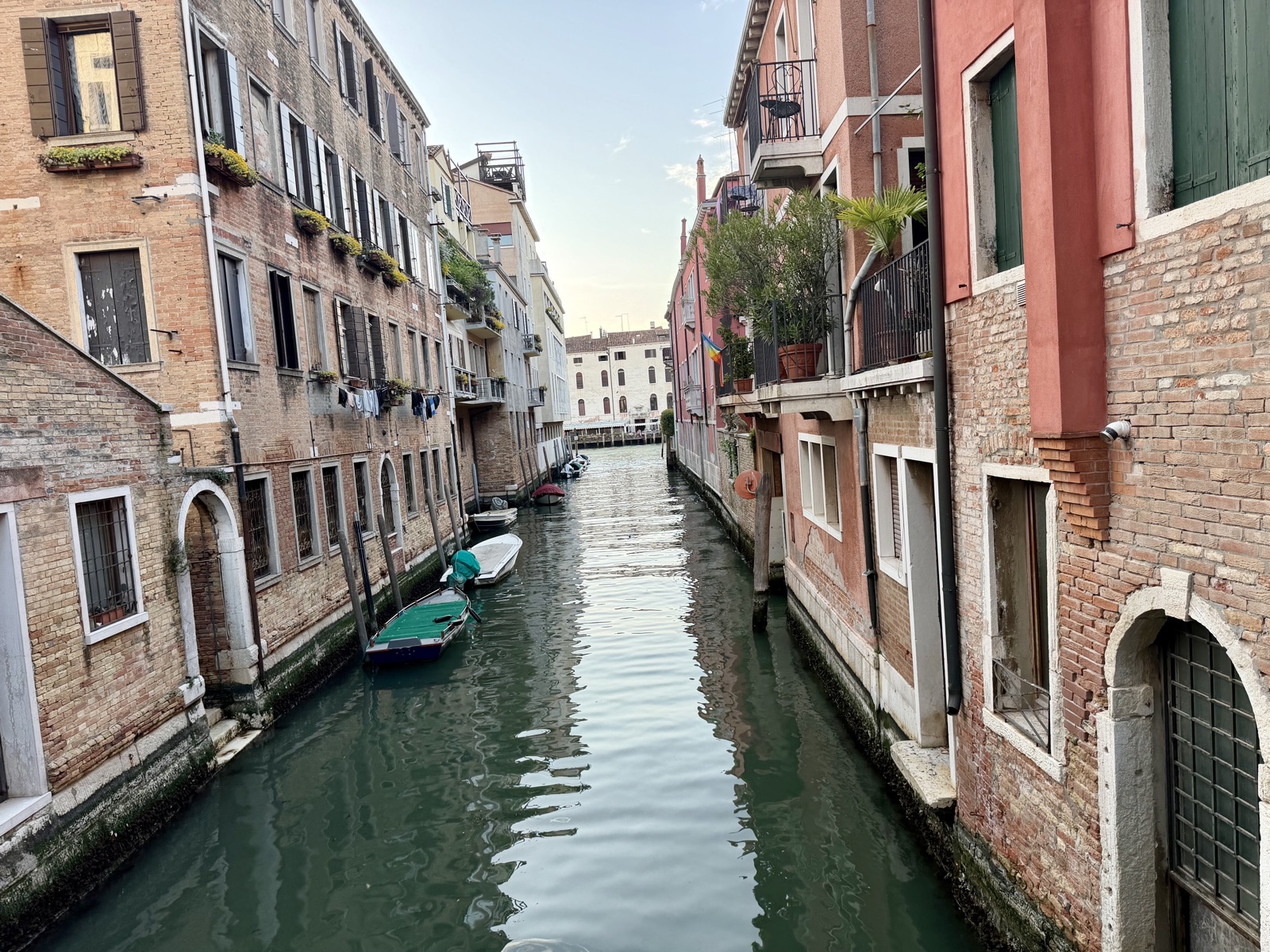 A quiet back canal in Venice with brick buildings, small boats, and laundry hanging on a line, the kind of Venice you find off the tourist trail