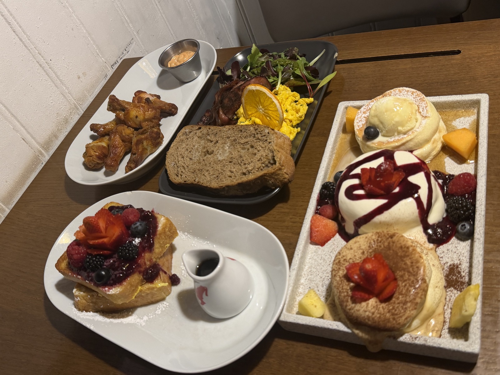 A brunch spread at Brunch Cafe in Venice with eggs, French toast piled with berries, chicken wings, bread, and pancakes