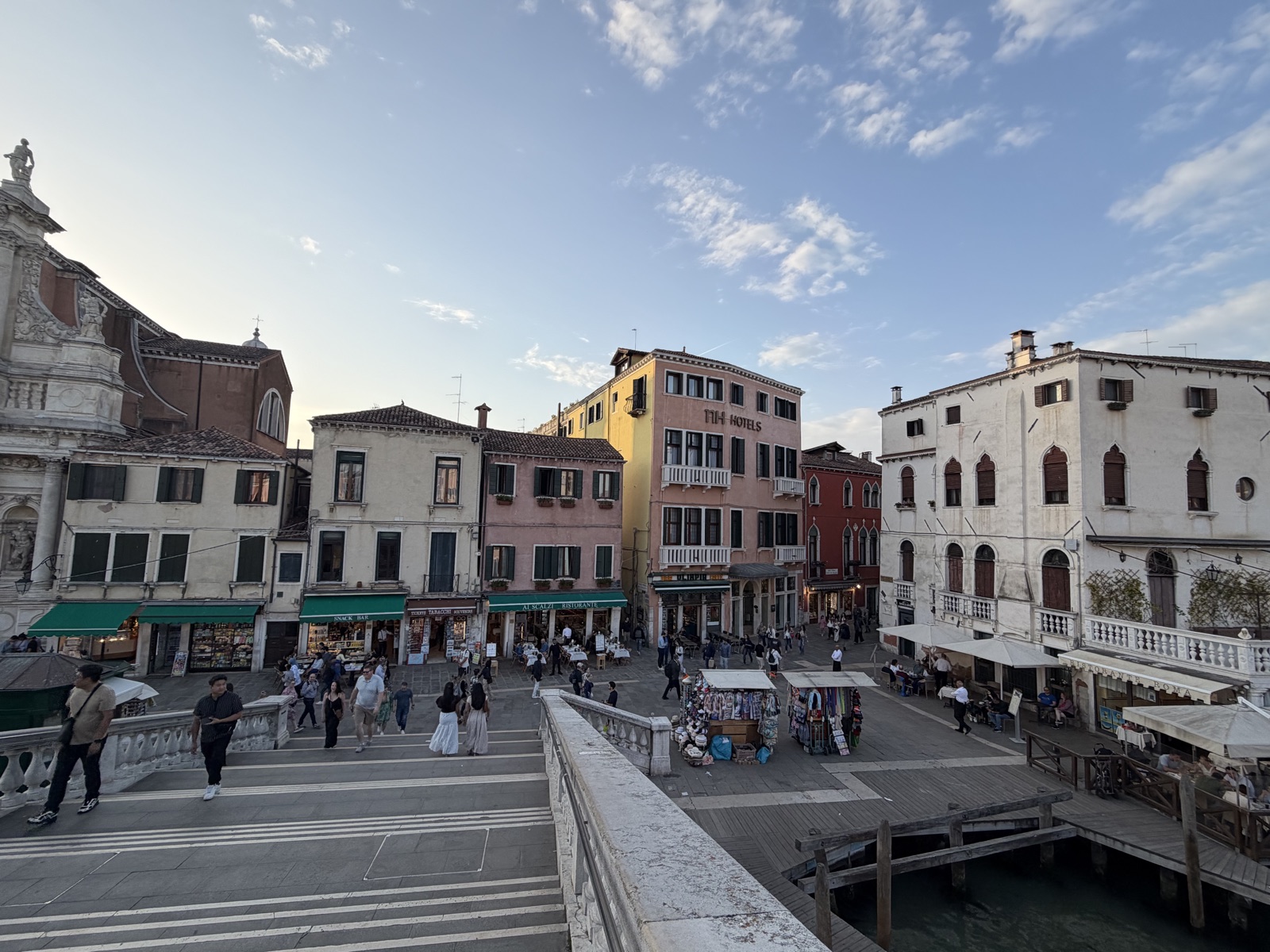 A small Venice piazza at golden hour, with people walking past shops and restaurants